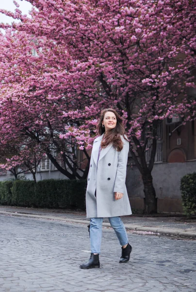 Gülümseyen esmer bir kadın baharda sakura ağaçlarıyla sokakta yürüyor.