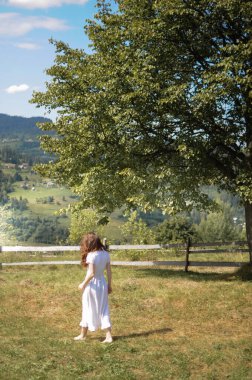 Beyaz elbiseli çıplak ayaklı bir kadın çimlerin üzerinde yürüyor.