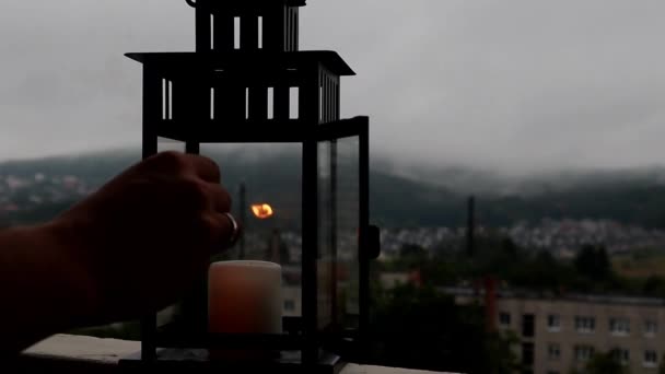 Man is set fire on candle in lantern on the terrace. Cloudy background. — Stock video