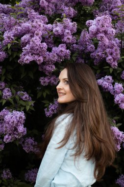 A young beautiful brunette woman near lilac flower blossom bush in springtime