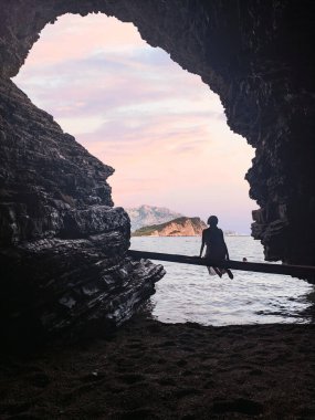 Silhouette of woman in a cave in front of a beautiful seascape and mountain view on Mogren beach in Budva, Montenegro
