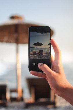 Gün batımında plaj şemsiyesi ve güneş yatağının fotoğraflarını çeken bir adam.