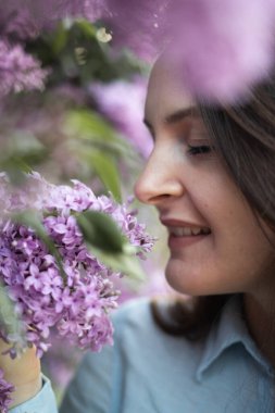 Genç, güzel, esmer kadın bahar vakti açan leylak çiçeklerini kokluyor.