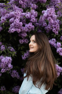 Young beautiful brunette woman is smelling lilac flower blossom in spring time