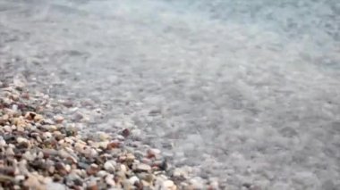 Dalgaların yakın çekim videosu taş bir çakıl taşı plajında dönüyor.