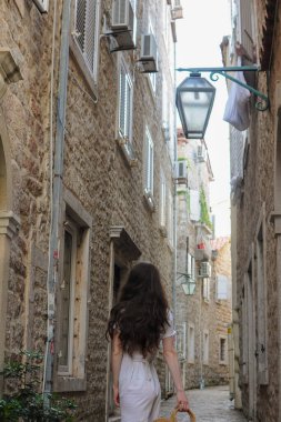 Karadağ 'ın eski Budva kentindeki taş binaları olan küçük bir sokakta gelinlik giymiş genç ve güzel bir kadın yürüyor.