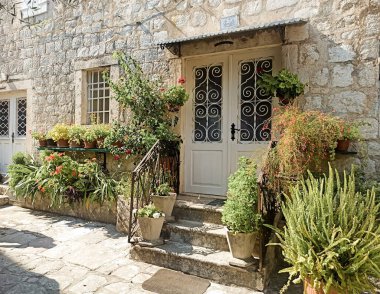 Karadağ 'ın eski Perast kentinde kapıları olan taş bina yakınlarındaki saksı bitkileriyle bahçeler.