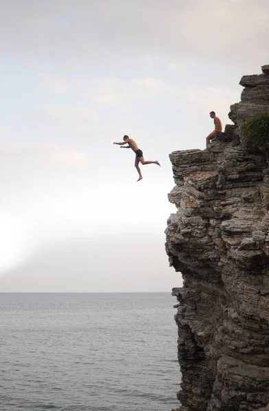 A man is jumping from a high cliff into the sea on a sunny day