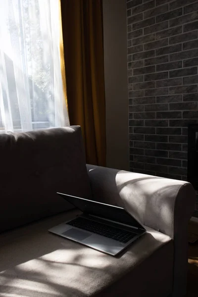 阳光灿烂的一天 一台打开的笔记本电脑躺在沙发上 漂亮的现代内部 没有人的概念 — 图库照片