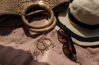 Plaj aksesuarlarının en üst görüntüsü: hasır şapka, yaz çantası, güneş gözlüğü ve yaz günü kumsalda yatak örtüsü üzerinde küpeler. 