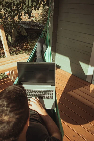 A top view of a man working in a hammock near a cottage. on a sunny day. Vacation and travel. Distant work, freelancer, blogger. Vacation and travel.