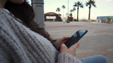 Arka planda palmiye ağaçları olan açık deniz kenarında akıllı telefon kullanan genç bir kadına yaklaş..