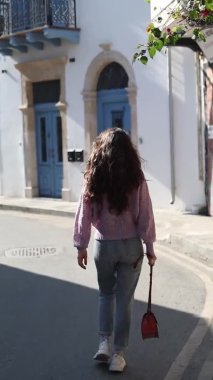 Arkadan mutlu genç bir kadın, Kıbrıs Rum Kesimi 'nin Larnaka kentinde mavi kapıları ve pencereleri olan güzel bir binanın yanında yürüyor..