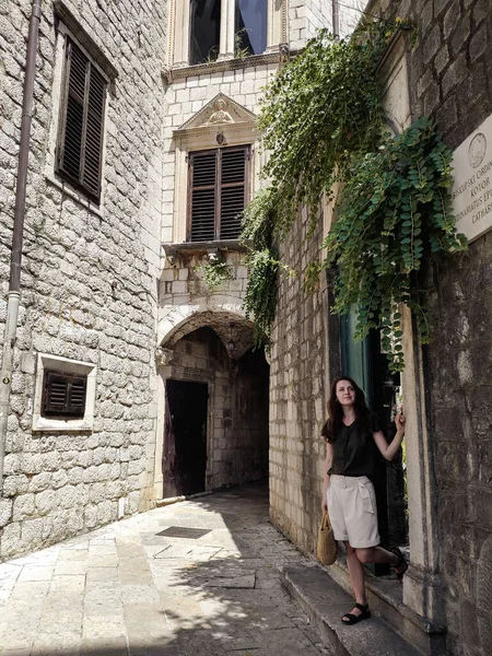 A young woman is walking in a tiny street with stone buildings in the old town of Kotor, Montenegro