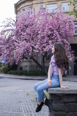 Esmer genç bir kadın baharda büyük bir sakura ağacının önünde oturuyor.