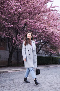 Gülümseyen esmer bir kadın baharda sakura ağaçlarıyla sokakta yürüyor.
