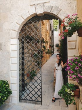 Karadağ 'ın Perast kentindeki büyük kapıları ve saksı bitkileriyle küçük bir sokakta yürüyen elbiseli genç ve güzel bir kadın görülüyor.