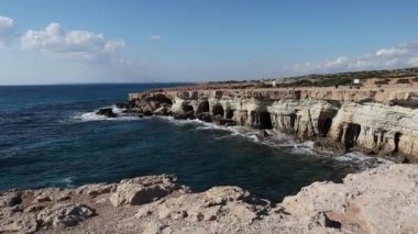 Kıbrıs Rum Kesimi 'nin Ayia Napa kentindeki turkuaz su denizi olan bir milli parktaki Cape Greco yakınlarındaki deniz mağaralarının güzel manzarasının önünde yürüyen bir adam görülüyor.. 
