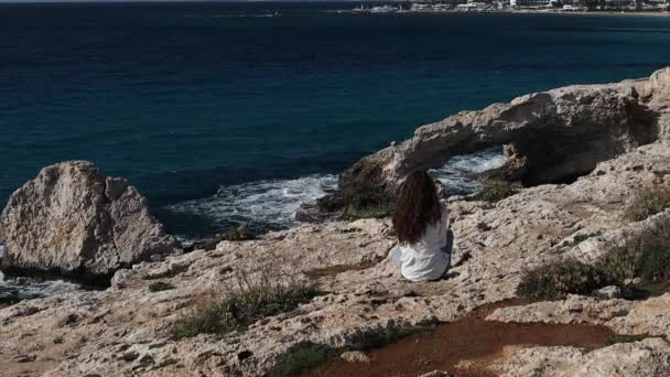 海の洞窟の近くの端に一人で座っている後ろから若い屈託のない女性は キプロスのAyiaナパの愛の橋 — ストック動画