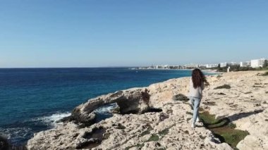 Arkadan kaygısız genç bir kadın deniz mağaralarının kenarında yürüyor Kıbrıs Rum Kesimi Ayia Napa 'da aşk köprüsü