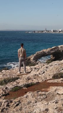 A young man from behind is standing on the edge of the sea caves love bridge in Ayia Napa, Cyprus
