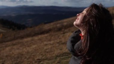 A young brunette woman with closed eyes is enjoying a mountains view. The girl is smiling in a beautiful sunny day in autumn