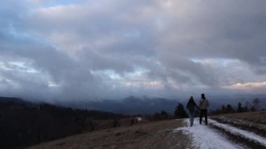 A young couple from behind is walking together on a winter snowy road in the Carpathian mountains