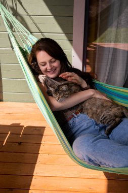 Kadın köydeki evin yakınındaki bir hamakta yatarken kedinin kafasını okşar.