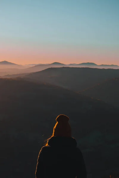 A young woman from behind is standing and looking away at the mountains\' autumn landscape in the morning