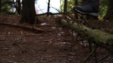 A woman in hiking boots oversteps a tree in the forest. Close up of girls feet in winter trackers walking outdoors.