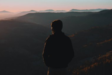 Arkadan genç bir adam duruyor ve sonbahar sabahları dağlara bakıyor.