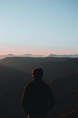 Arkadan genç bir adam duruyor ve sonbahar sabahları dağlara bakıyor.