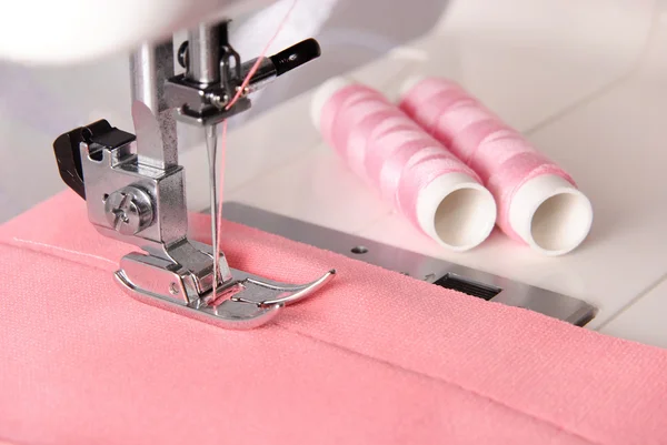 Процесс шитья розовой ткани на машине и два боббинса — стоковое фото