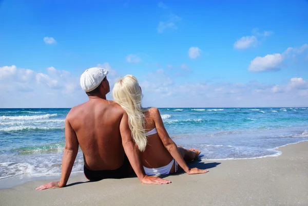 Loving couple sitting on sea sand beach and look at the blue sky — Stock Photo, Image