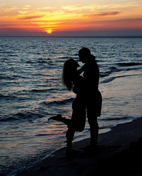 Silueta de pareja en la playa contra la puesta de sol — Foto de Stock