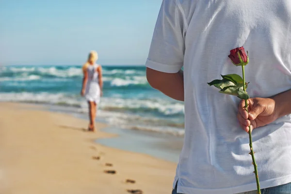 Любящая пара, мужчина с розой ждет свою женщину на морском пляже — стоковое фото
