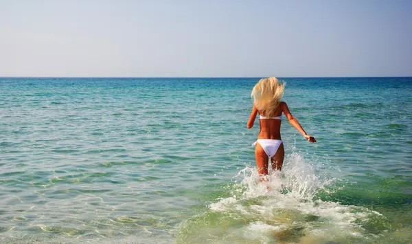 Schöne schlanke junge Frau läuft im Sommer in den Wellen des Meeres — Stockfoto