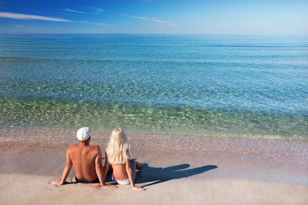 Pareja amorosa sentada en la playa de arena marina y mira el azul —  Fotos de Stock