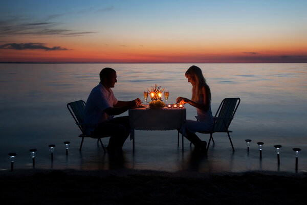 A young couple share a romantic dinner with candles on the beach