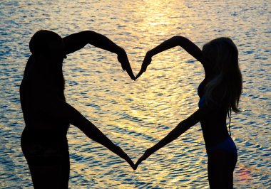 Genç çift sunse karşı plaj üzerinde kolu olan kalp şekil verme