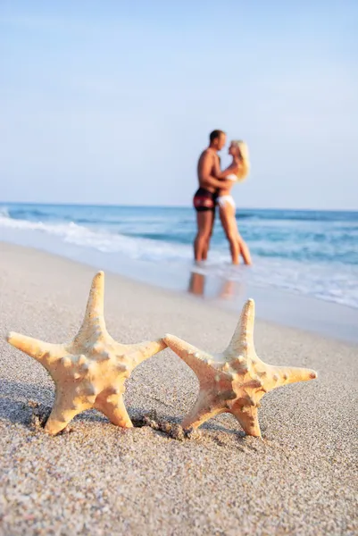 Couple hug on sea sand beach against starfishes — Stock Photo, Image