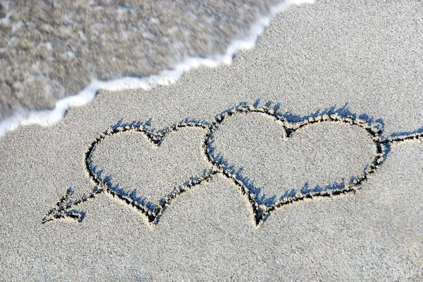 Dos corazones esbozan en la arena contra la ola — Foto de Stock