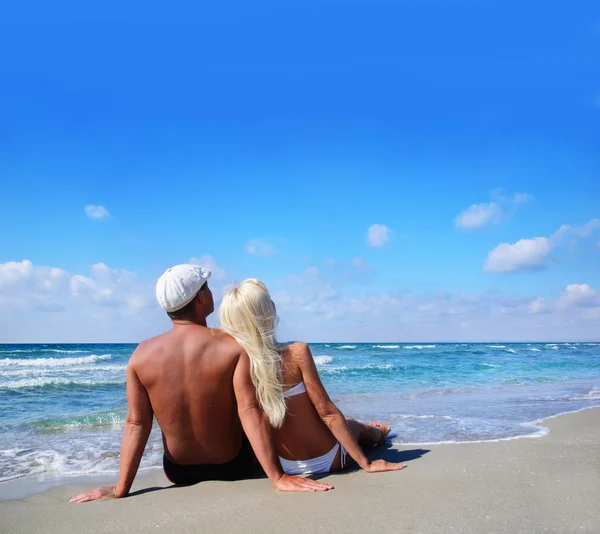 Loving couple sitting on sea sand beach and look at the blue sky — Stock Photo, Image