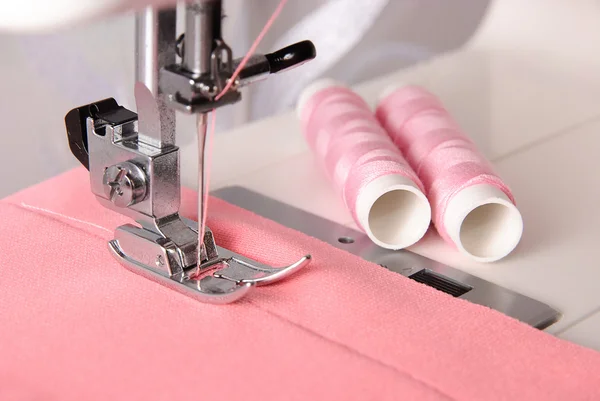 Naaien proces van rooskleurig doek op de machine en twee spoelkokers — Stockfoto