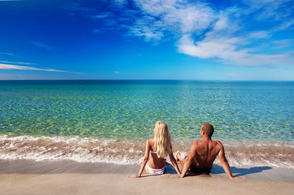 Jeune couple assis sur la plage de sable de mer et regarder le ciel — Photo