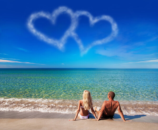 love concept - young couple on sea beach look at cloud heart