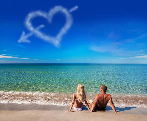 Love concept - young couple on sea beach look at cloud heart — стоковое фото