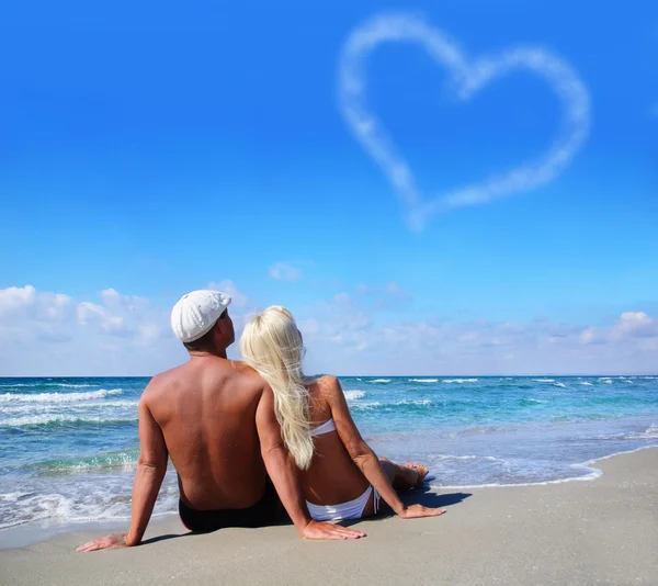 Láska koncepce - pár na mořské pláži pohled na oblačno srdce — Stock fotografie