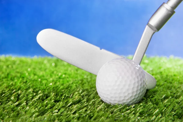 Golfbal en club op groene veld gras tegen blauwe hemel — Stockfoto