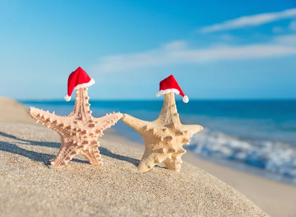 Coppia di stelle marine in cappelli di Babbo Natale a piedi sulla spiaggia. Concetto vacanza — Foto Stock